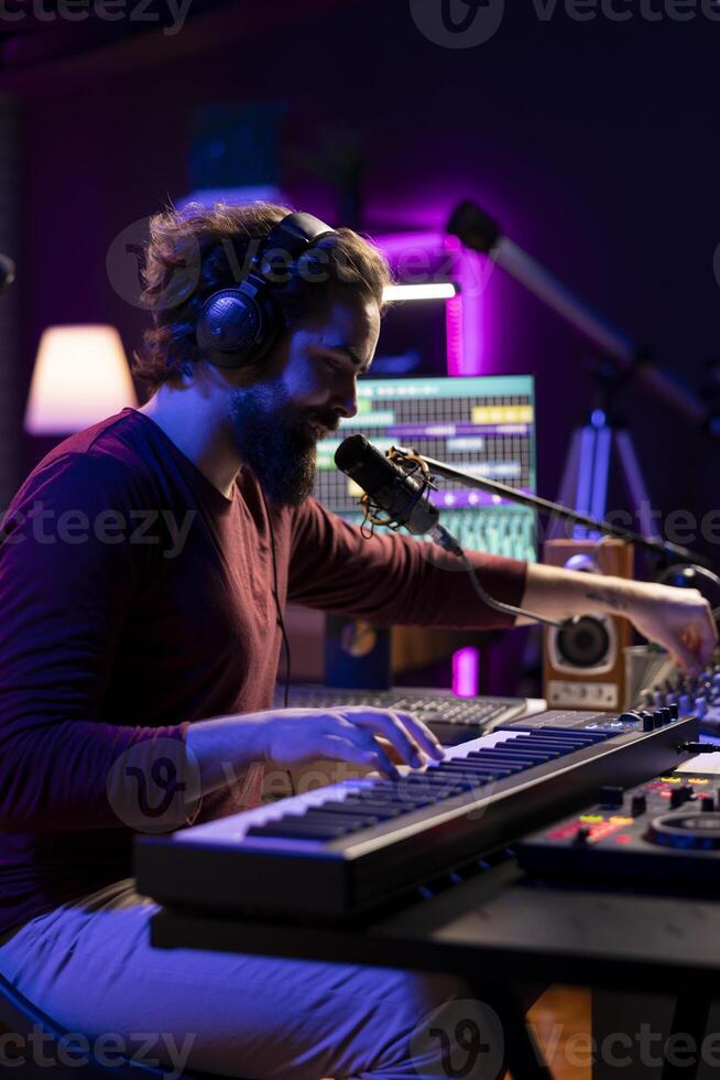 Audio engineer playing piano electronic keyboard to compose a new song, singing on microphone and adjusting volume levels. Producer recording music, plays on midi controller gear. photo