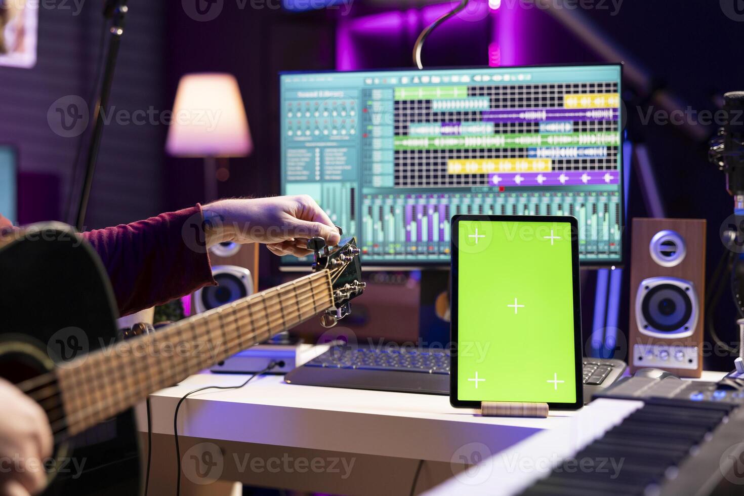 Artist songwriter practicing to play and tune his guitar by twisting knobs, watching online lesson via tablet with greenscreen display. Musician learning acoustic instrument skills in home studio. photo
