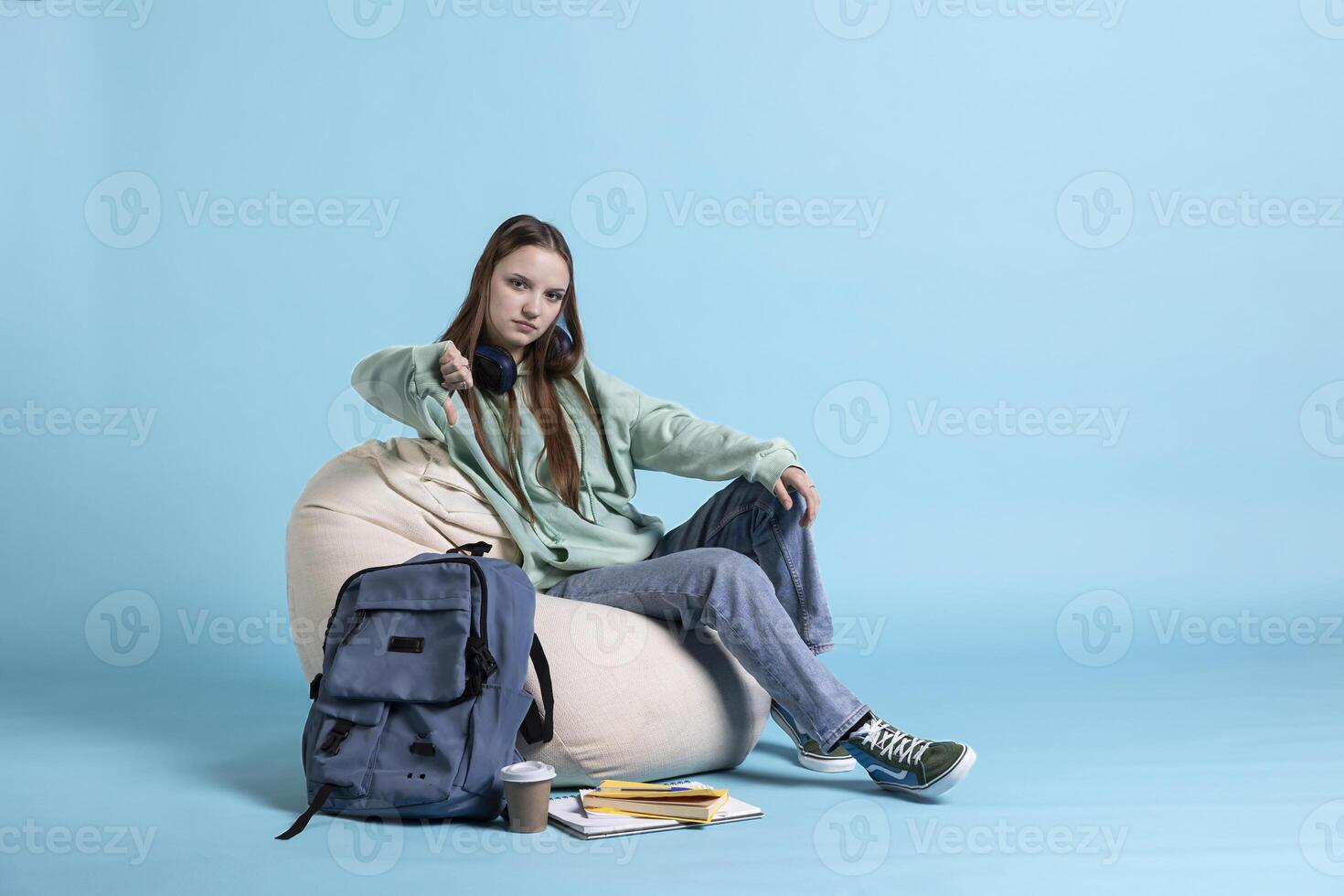 Portrait of schoolgirl showing thumbs down sign, annoyed for having to prepare for university exams, studio background. Teenager doing negative hand gesturing regarding difficult homework photo