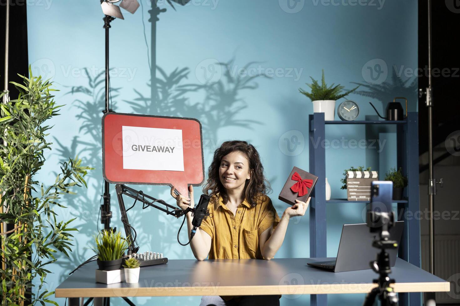 Cheerful vlogger advertising giveaway for viewers with cardboard sign, offering gift box, engaging with audience. Upbeat person organizing online contest, explaining rules using copy space board photo