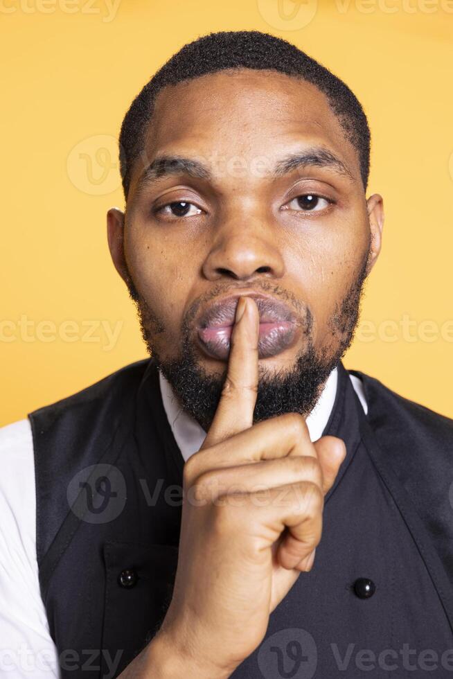 Restaurant waiter doing the hush mute gesture to be quiet and keep secret, covering his lips with his finger. Butler asking for privacy and secrecy, confidential information and no noise. photo