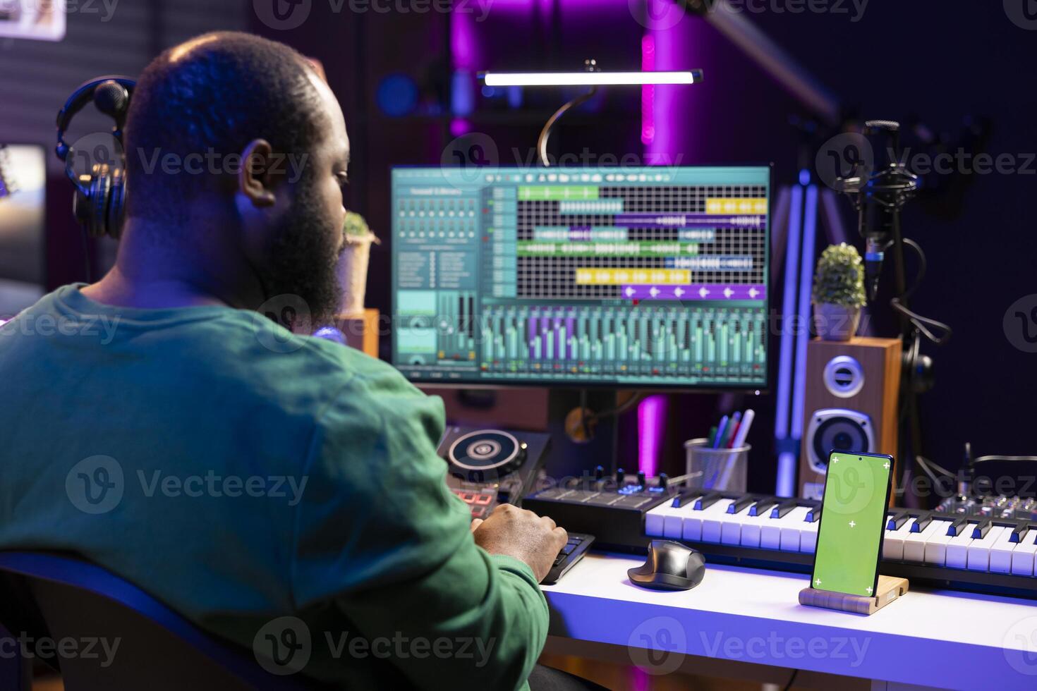 Songwriter working on making new music with a greenscreen on phone, operating on mixing console and professional software. Skilled artist producing and editing soundtracks in home studio. photo