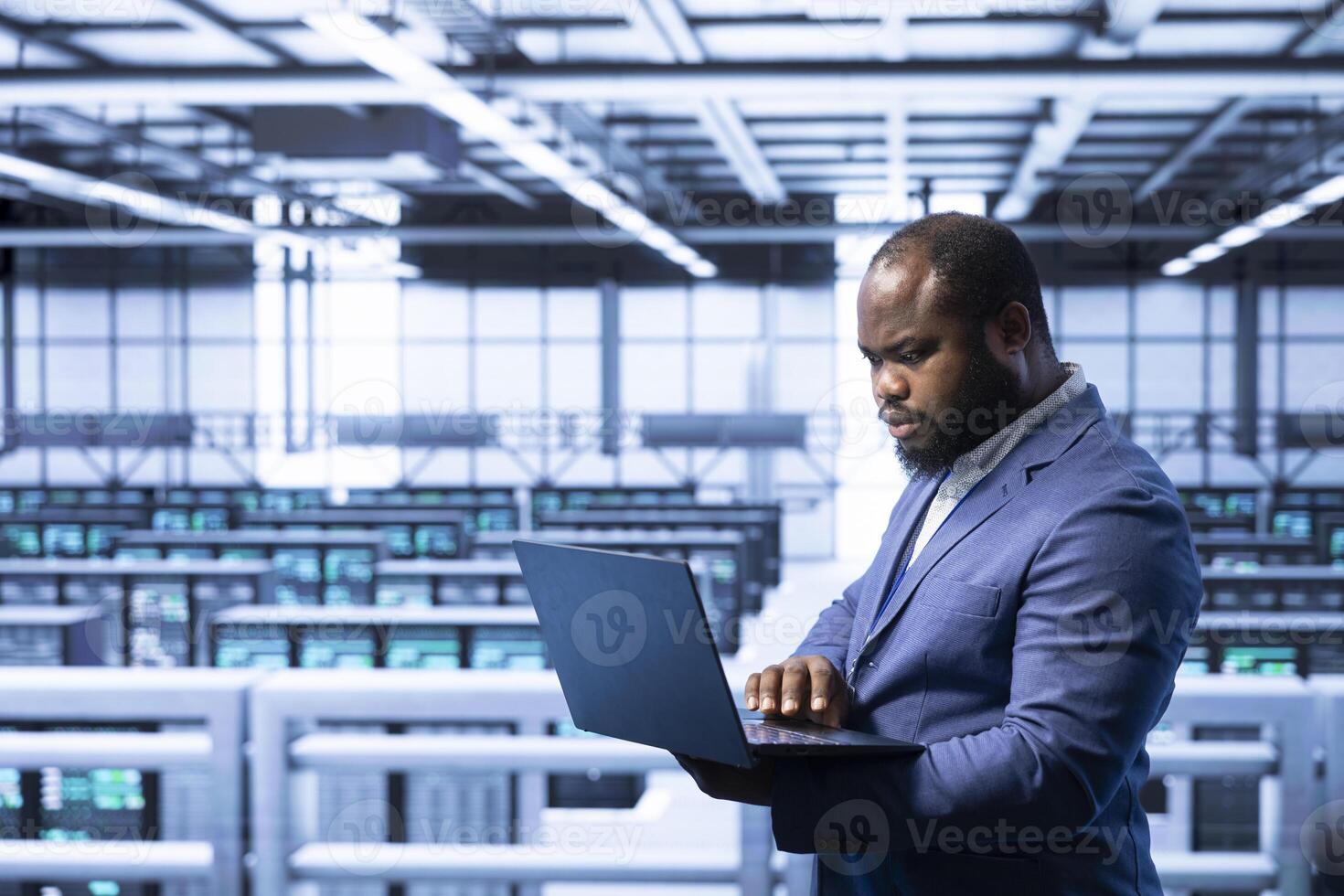 Worker in data center using laptop to configure network infrastructure such as routers, switches and firewalls. Data researcher working in server room, looking for technical malfunctions photo