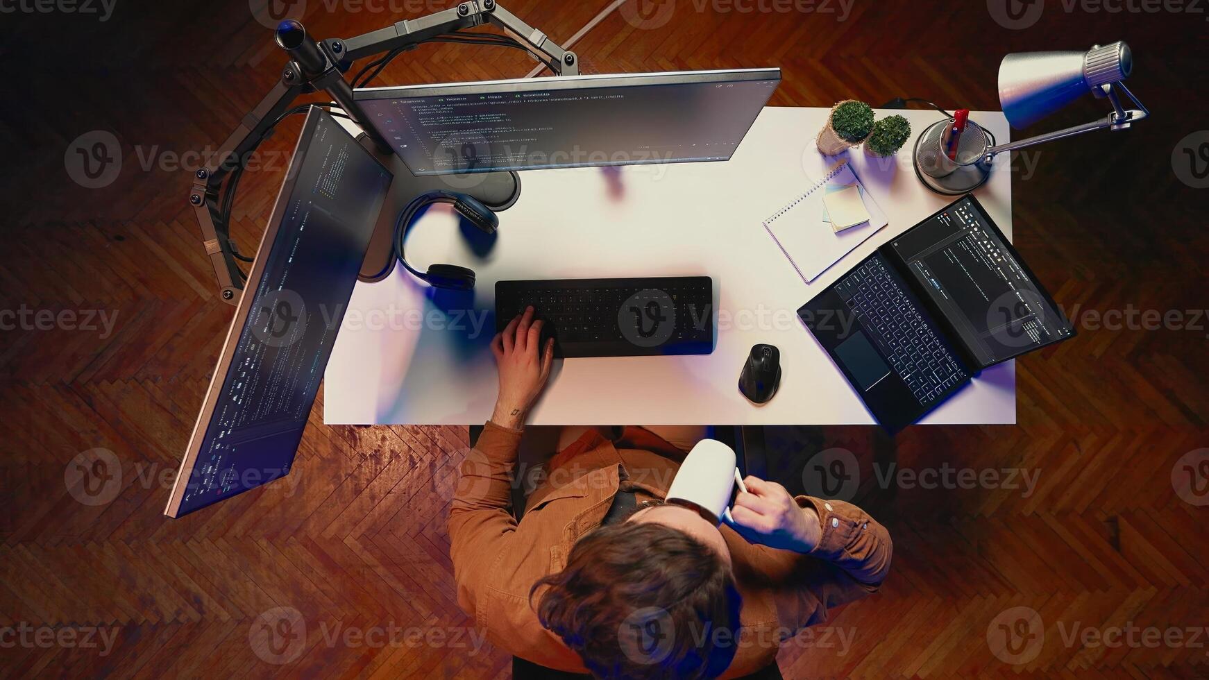 Top down view of self employed man doing IT support job from apartment personal office, coding on PC, drinking coffee. Software developer writing lines of code on computer at home, aerial shot photo