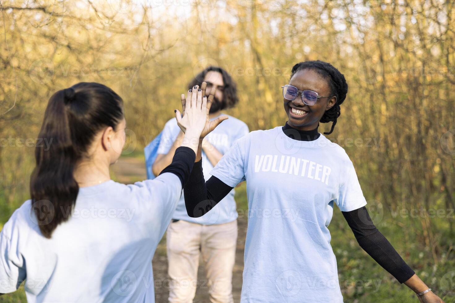 Satisfied diverse women sharing a high five feeling proud of their hard work to clean the natural habitat. Congratulating each other for showing perseverance and devotion. photo