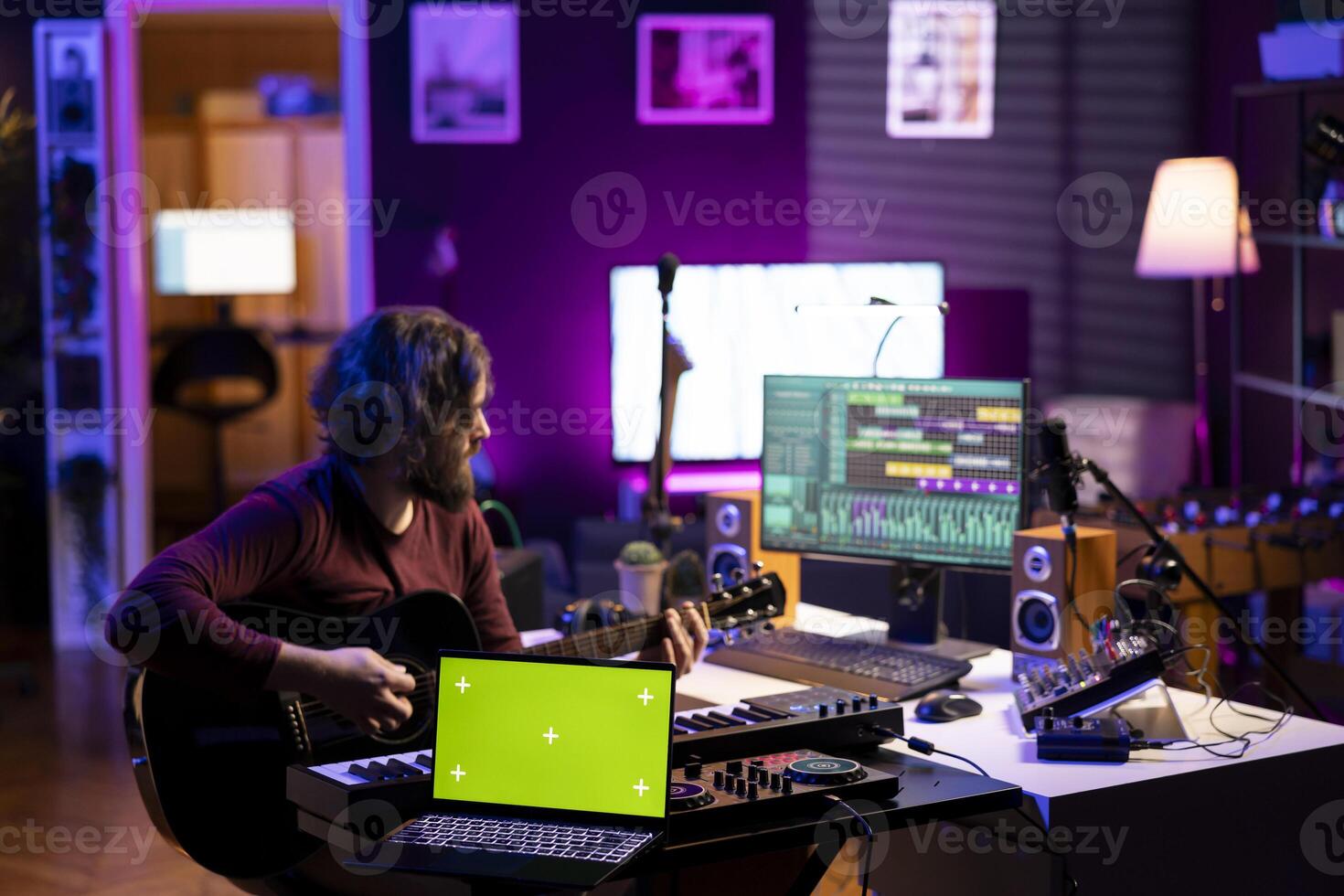 Sound engineer playing guitar next to laptop showing greenscreen display, recording songs with mixing console and daw software interface. Producer composes new music on acoustic instrument. photo