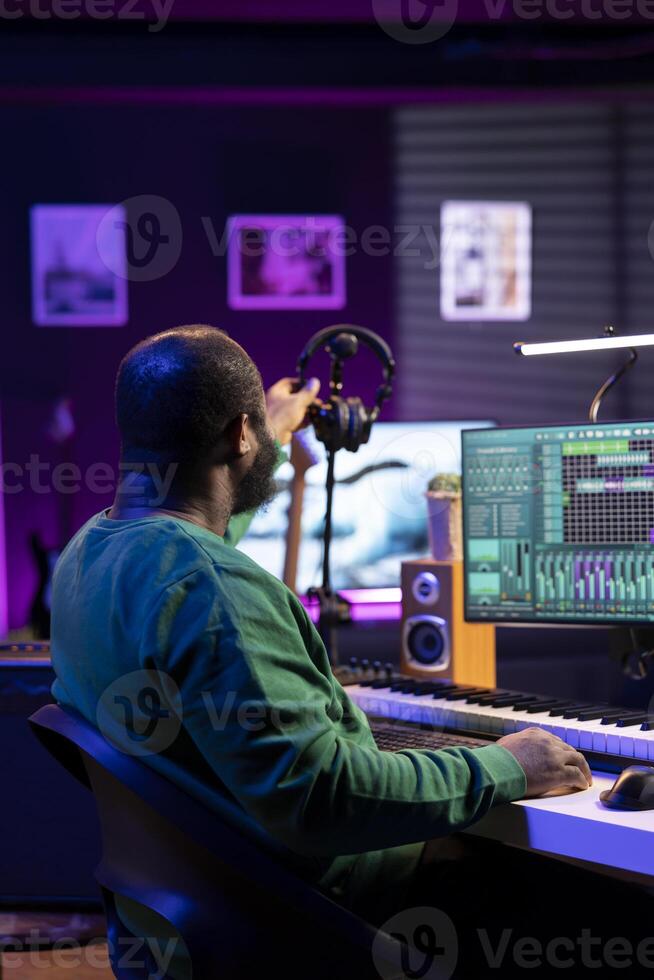 Sound producer working with console and electronic keyboard to create the perfect tracks for his songs, recording and editing audio. Music composer adjusts volume levels on pre amp knobs. photo