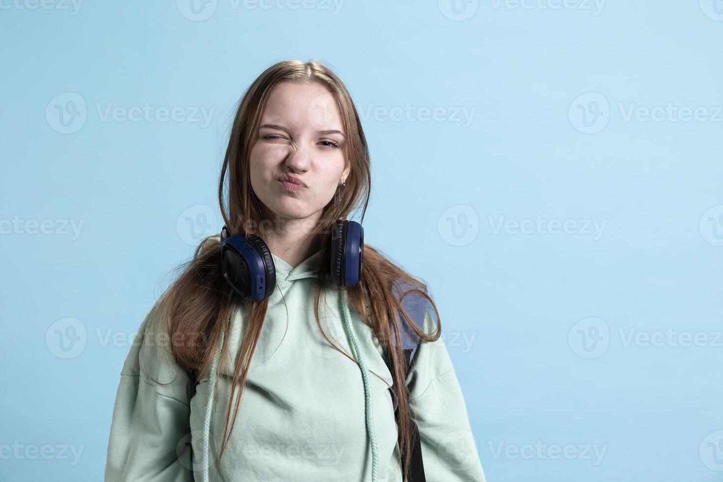 Young person doing goofy childish facial expressions, acting amusing and playful, isolated over studio background. Childish teenager making quirky faces, entertaining herself photo