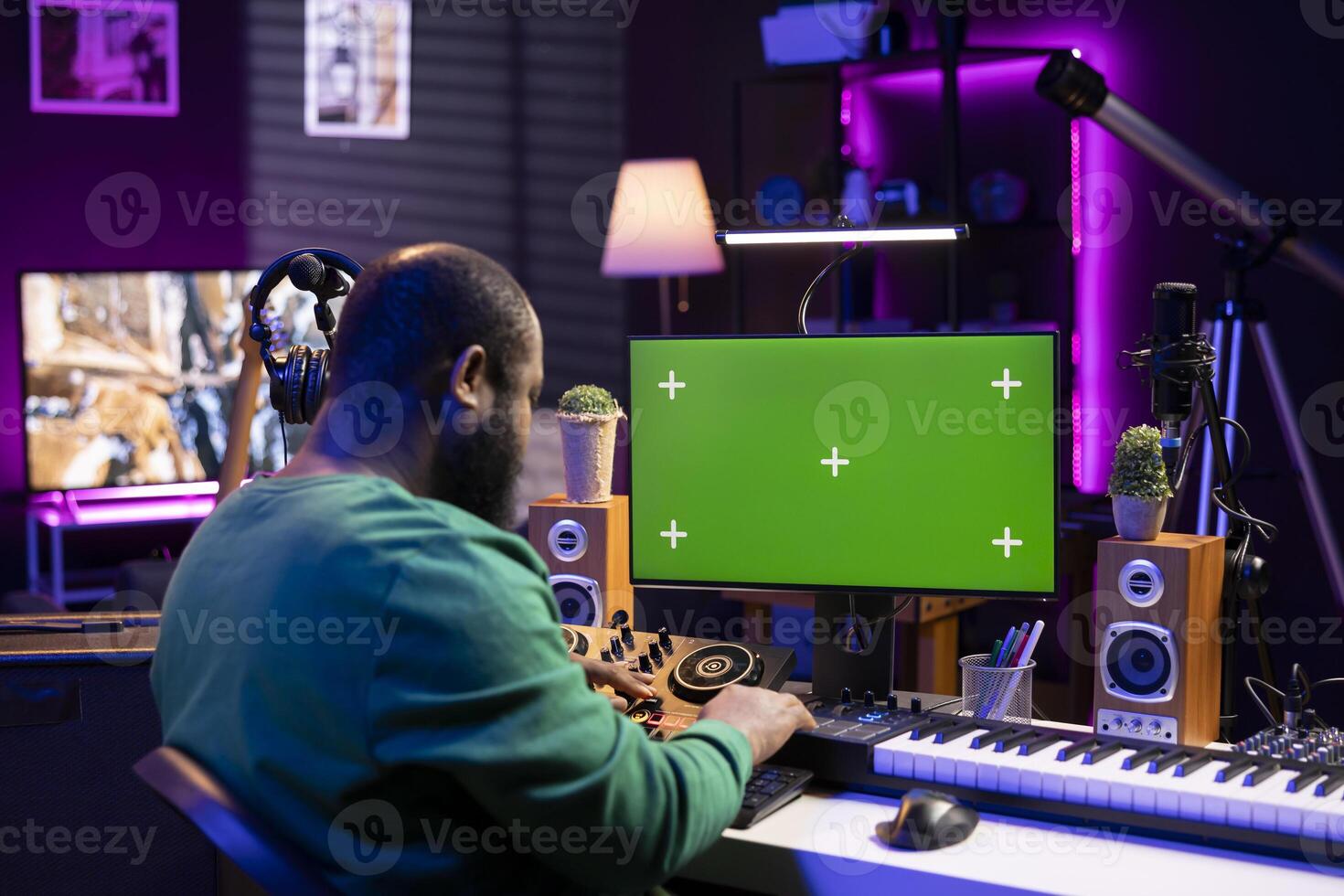 African american producer creating new sounds for a track, mixing audio files with console and synthesizer next to greenscreen. Technician producing soundtracks for a new album, stereo gear. photo