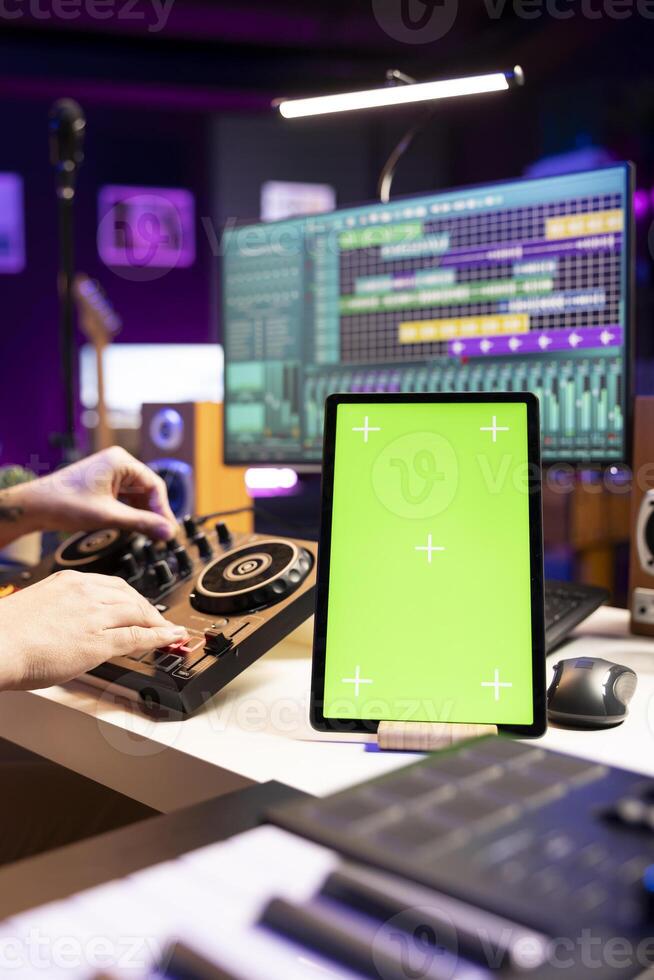 Producer editing soundtracks on stereo tools and greenscreen layout on tablet, mixing and mastering songs in home studio. Young musician adjusting volume levels on music, daw software. photo