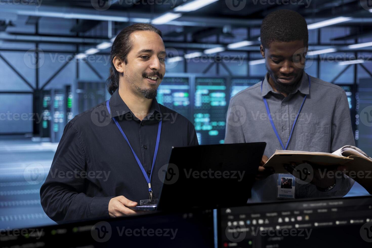 Cheerful IT specialists in server hub ensuring data remains shielded from potential threats. Smiling coworkers safeguarding data center against unauthorized access using laptop photo
