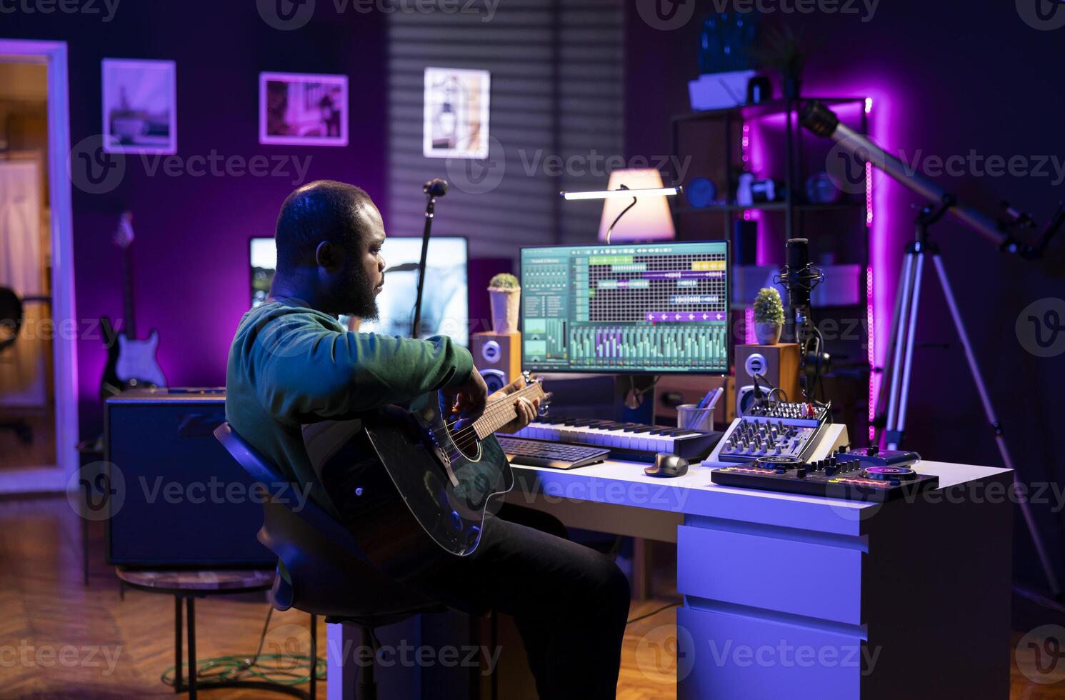 Producer creating a track by playing acoustic guitar in home studio, recording songs and singing on microphone. Sound engineer mixing and mastering his melody with stereo gear, soundtracks. photo