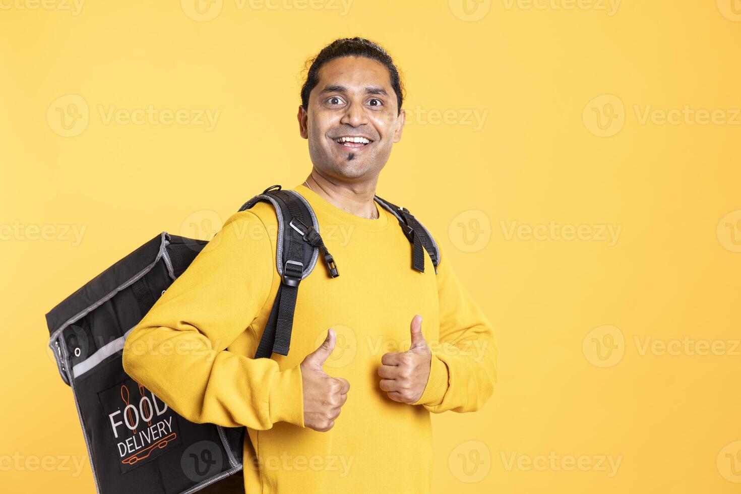 Portrait of cheerful man with thermal backpack doing thumbs up sign and smiling, excited to do job, studio background. Happy delivery person doing like hand gesture, going to client adress photo