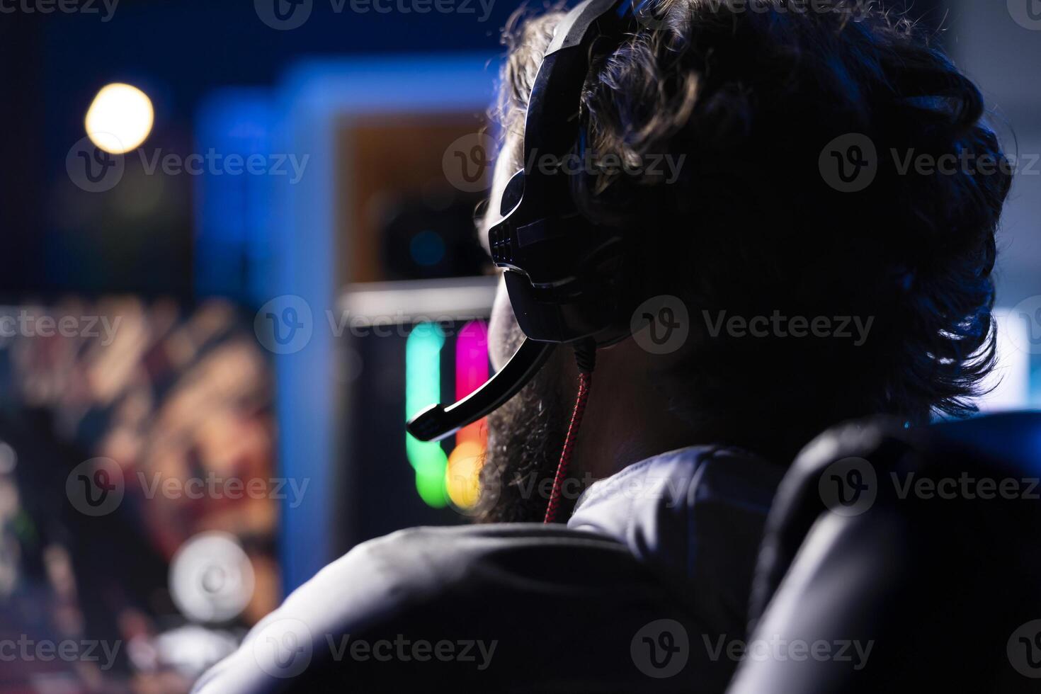 Man chatting with teammates online while playing games on gaming PC, relaxing after work. Close up of gamer battling enemies in online multiplayer shooter, talking through headphones mic photo