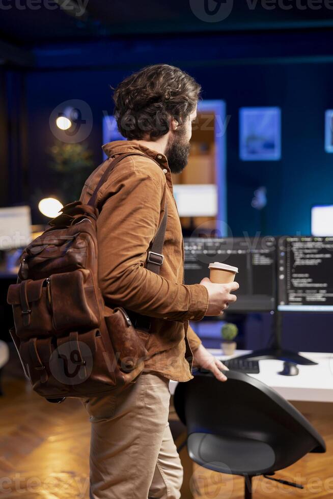 Programmer with disposable cup of coffee entering office to implement security measures, protecting company systems and data. IT worker starting job shift, testing and debugging code photo