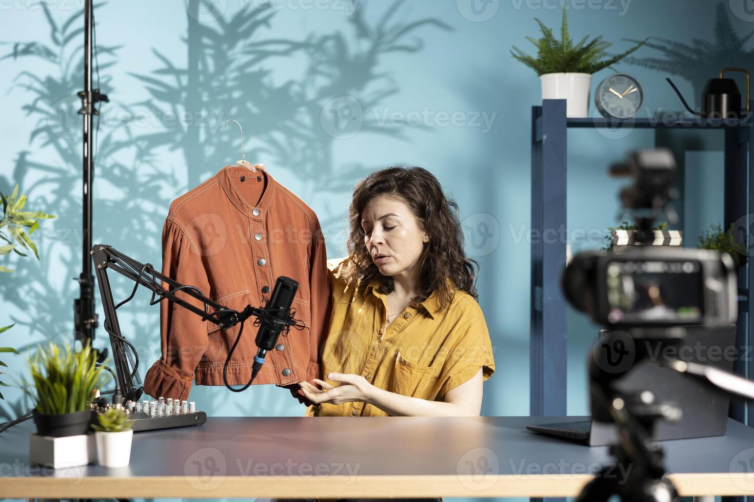 Media star holding orange jacket in hand, showing fans purchases she recently got, filming herself in studio. Content creator in studio presenting audience new acquisitions photo