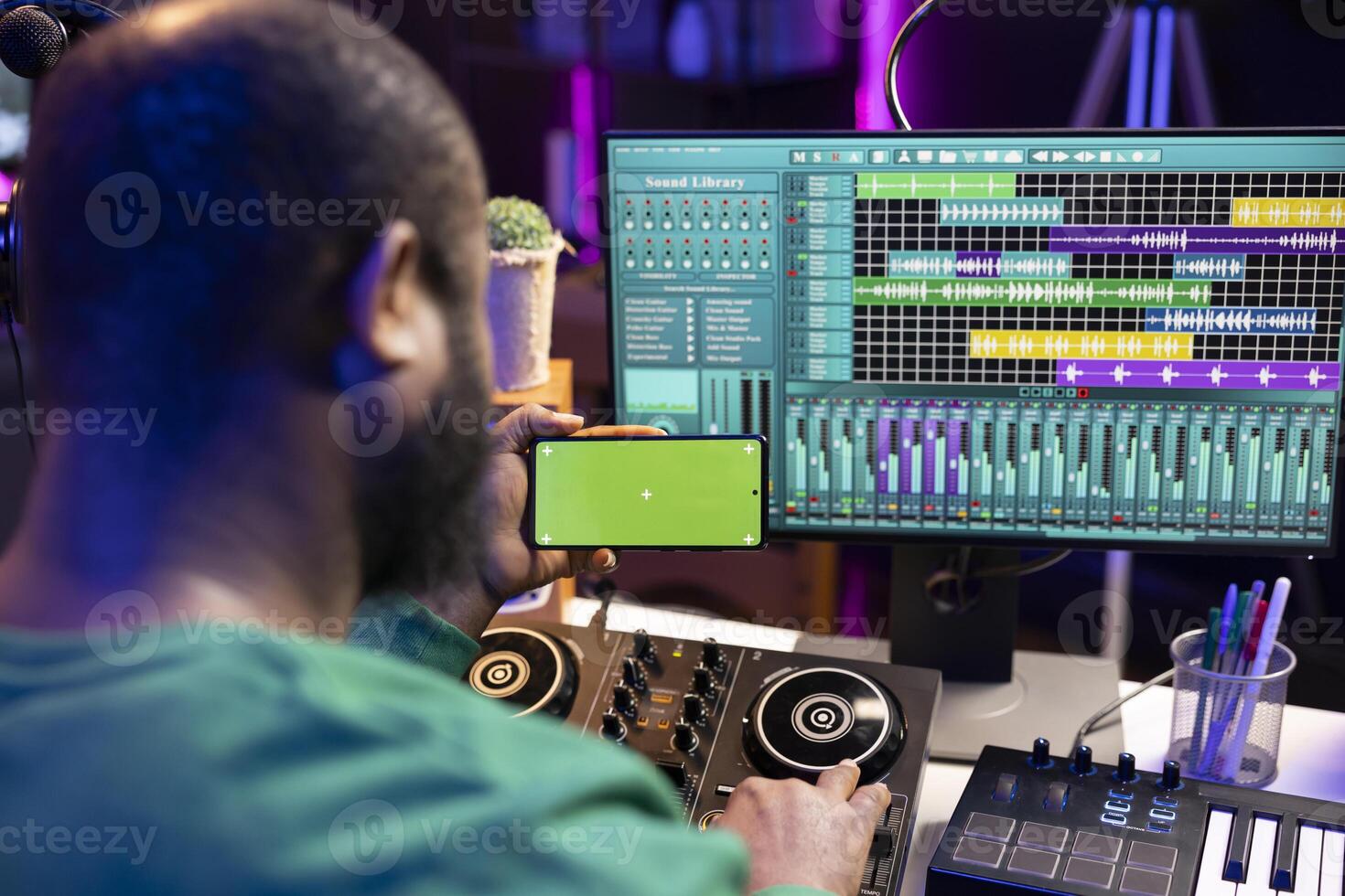 African american audio technician recording and editing tunes with pc software, looks at mockup chromakey display. Artist singer producing sounds for his new music, home studio. photo
