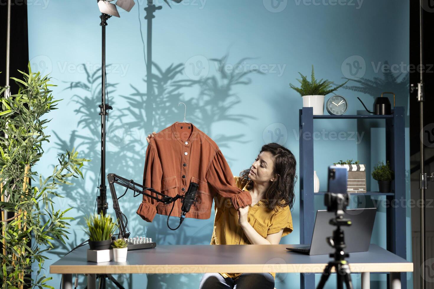 Content creator presents fast fashion jacket to viewers, filming haul with smartphone on tripod and mic. Fashion vlogger engaging subscribers with shopping haul, doing affiliated marketing photo