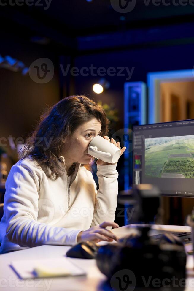 editor starting work on film montage, drinking beverage, using specialized software applications on PC. Freelancer in personal studio with cup of coffee, cutting project footage photo