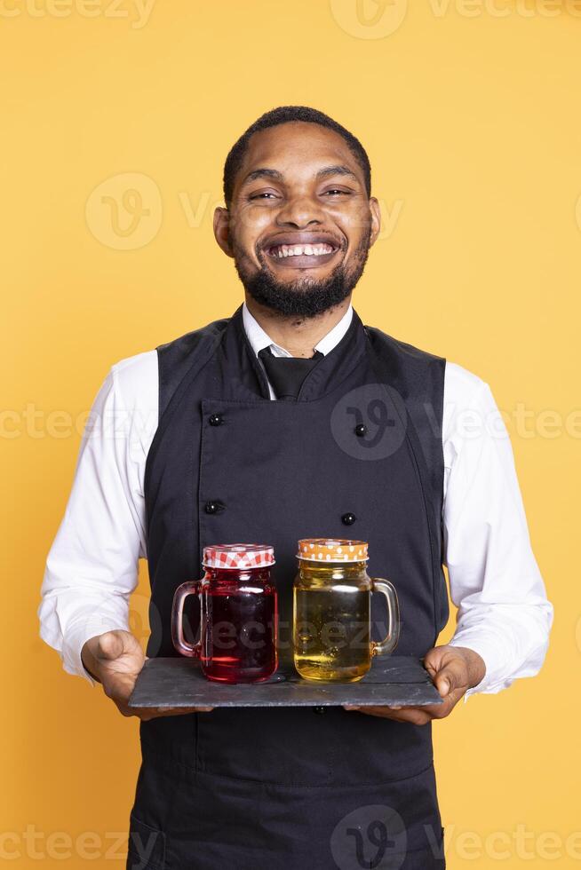Butler carrying a tray with glasses of drinks for clients at a table, serving fresh lemonade to customers before their dinner. Skilled waiter serving people at a five star restaurant. photo