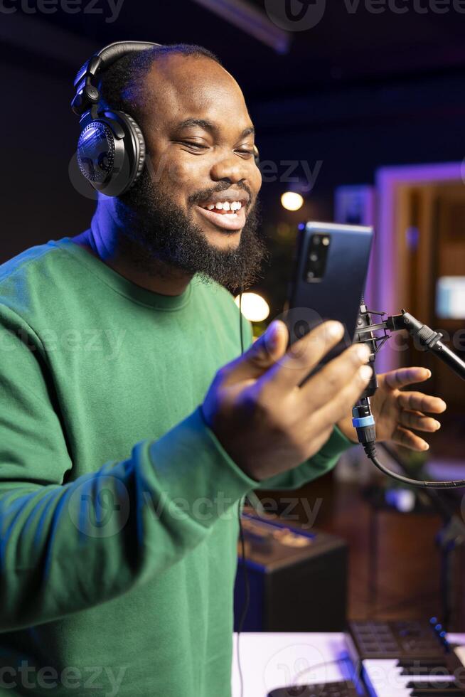 Happy musician singing his new musical creation on microphone, recording audio files to edit them in post production. Young artist songwriter reading the creative verses and elements on phone. photo