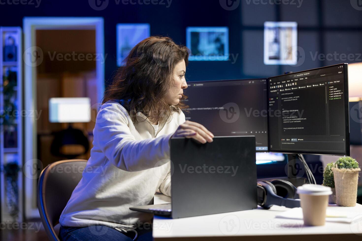 Teleworking software developer working from home opening laptop to write programs in Java programming language. Woman checking code displayed on computer screen, sitting at desk chair photo