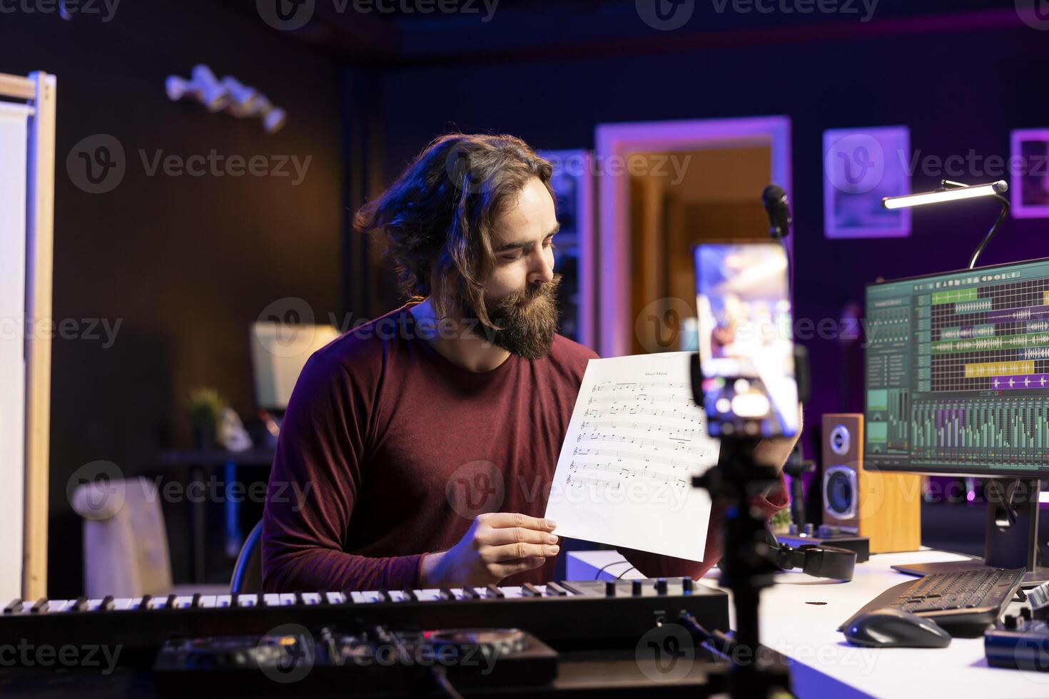 Young singer pointing at music sheet to explain notes on synthesizer, teaching people how to play piano electronic keyboard in home studio. Artist performer playing midi controller keys, online vlog. photo