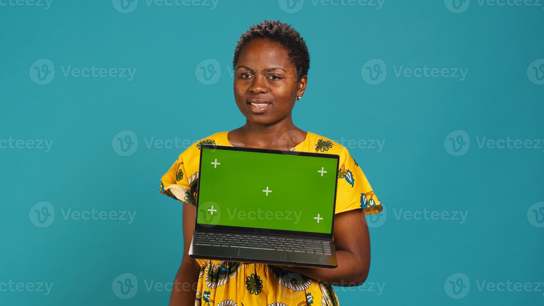 Natural smiling woman posing with a green screen on laptop, making an advertisement with isolated mockup display in studio. Young traditional person in tribal native clothing. Camera A. photo
