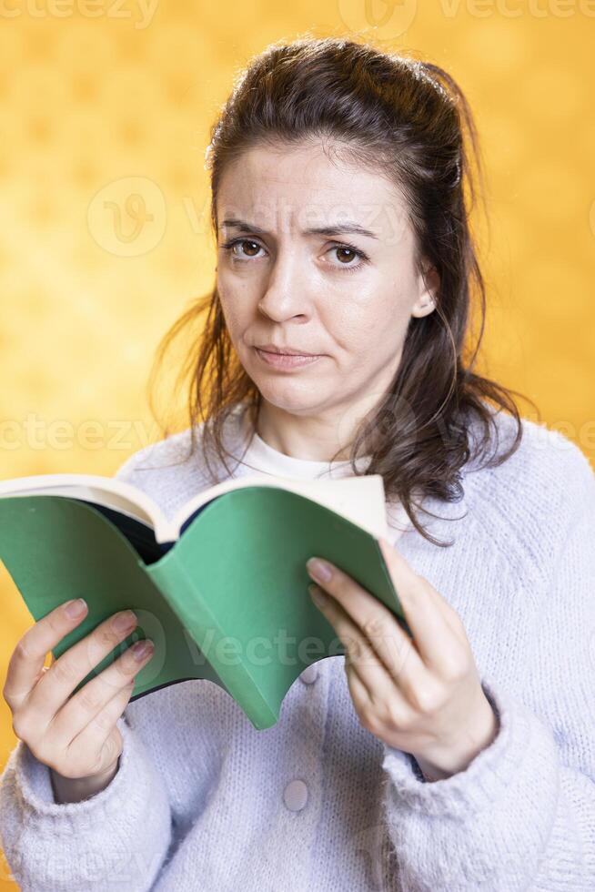 Woman frowning while reading book, upset by story, spending time on hobby. Bookaholic person with novel in hands critical of plot and characters, enthralled by emotional story, isolated over studio background photo