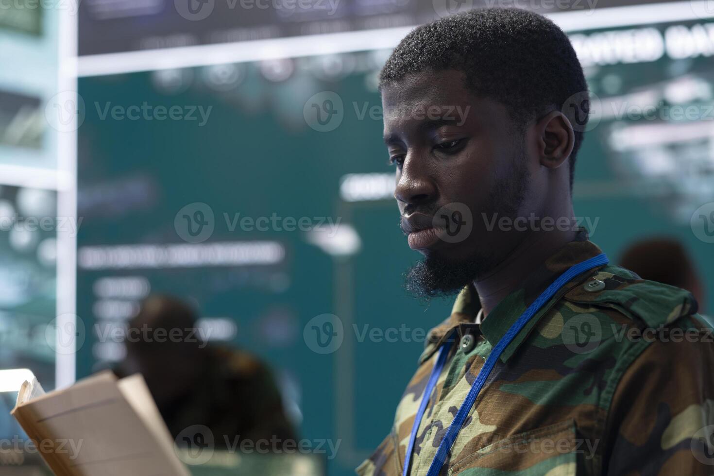 Army soldier reading a new defense operation case file in military headquarters, using reconnaissance CCTV footage on a big screen. Recruit tracking location of deployed troops. Close up. photo