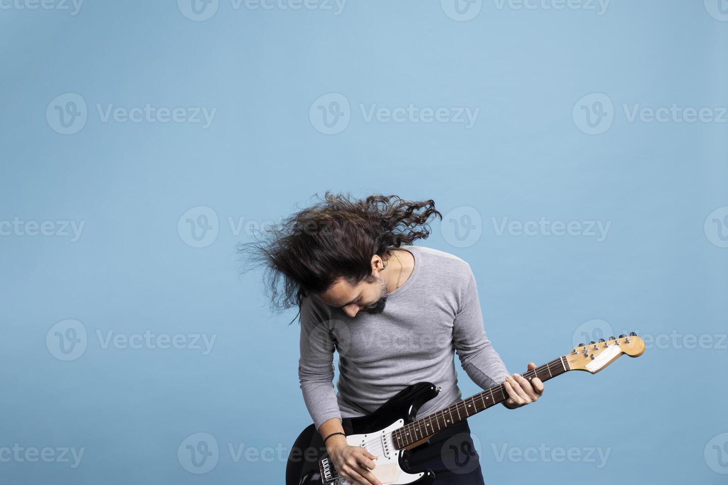 Enthusiastic rocker playing a black electric guitar with passion and joy for rock and roll music. Dynamic, trendy performer with long hair brings movement, fun and entertainment to the studio. photo