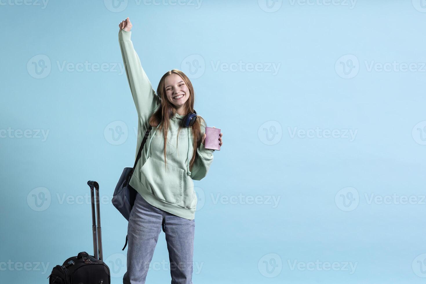 Cheerful young traveler holding passport, celebrating after arriving at destination, enjoying going on vacation. Jolly girl throwing hands up in excitement while travelling, studio background photo