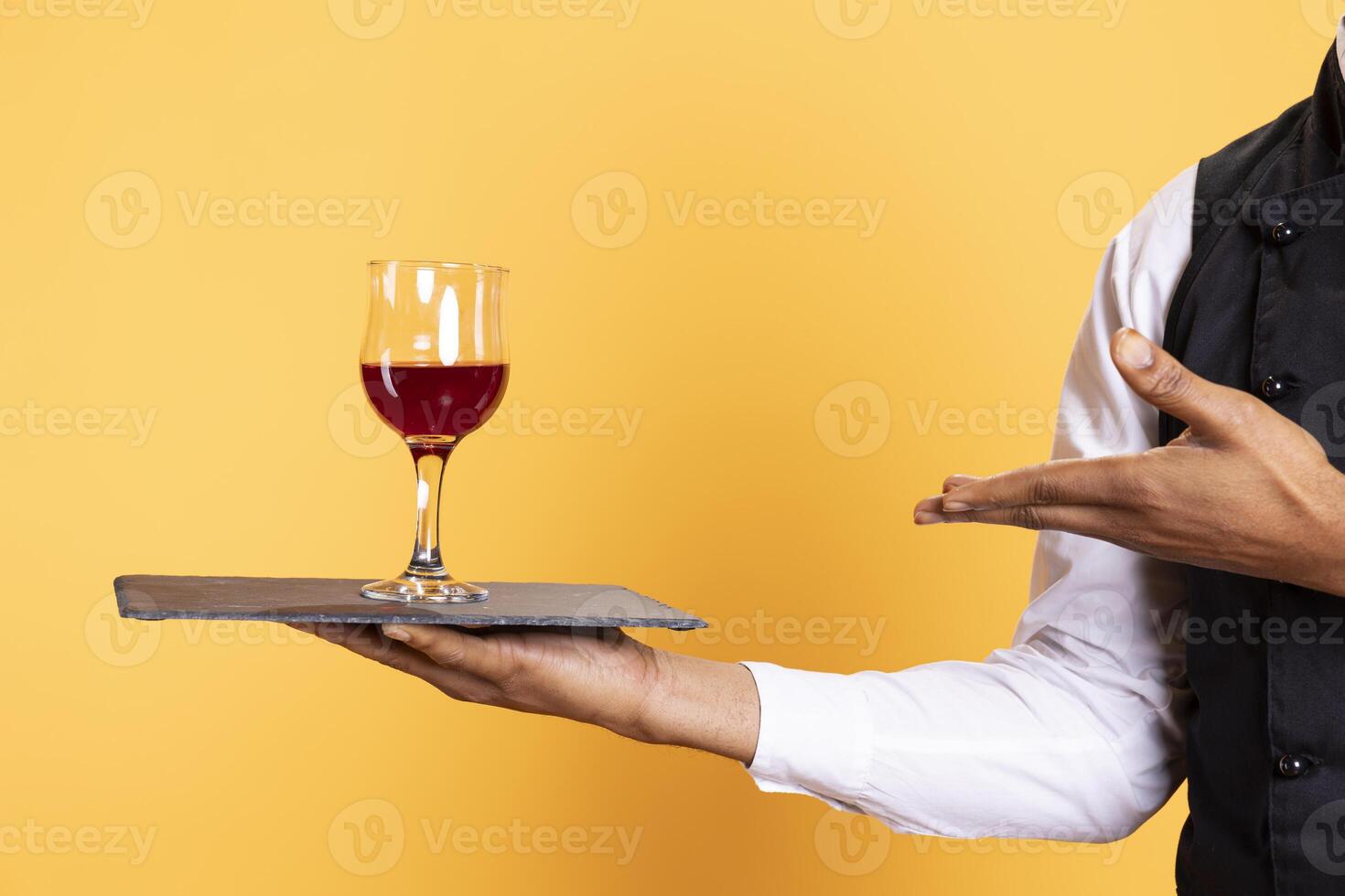 Waiter offering a glass of wine to customers waiting for their food at the table, providing excellent service at a restaurant. Professional staff with uniform bringing drinks to clients. photo