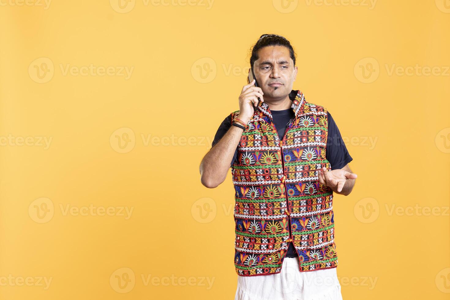 Dissatisfied man wincing after listening dumb opinions from friend during cellphone call. Person wearing traditional indian clothes in disagreement with mate, studio background photo