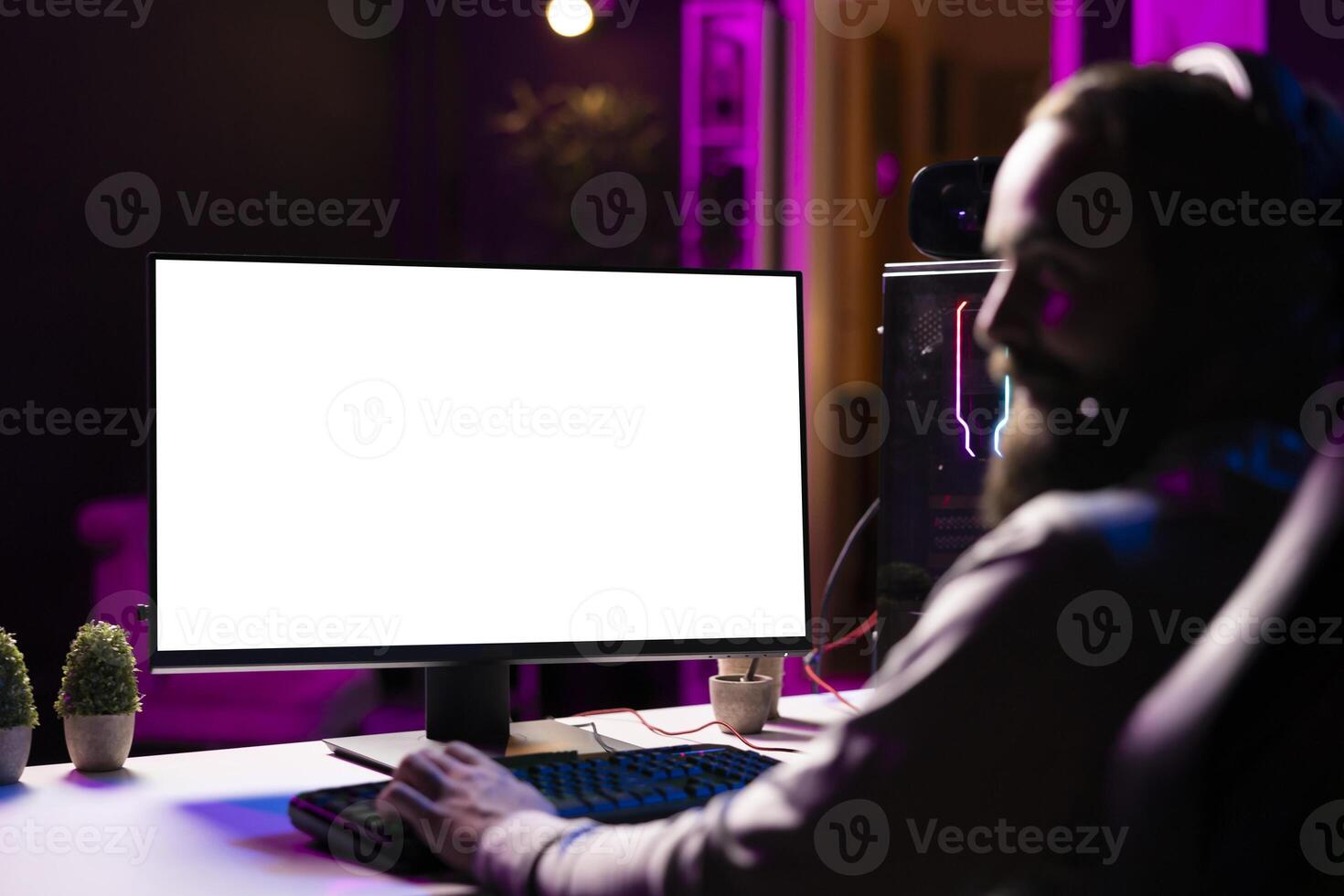 Man in dimly lit apartment playing games on isolated screen gaming PC at computer desk, enjoying day off from work. Gamer battling enemies in online multiplayer shooter on mockup display photo