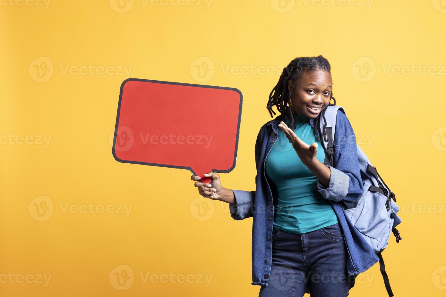 Joyful young girl showcasing red speech bubble sign of empty copy space for message. Happy african american teenager presenting thought bubble cardboard used as promotion concept, studio background photo