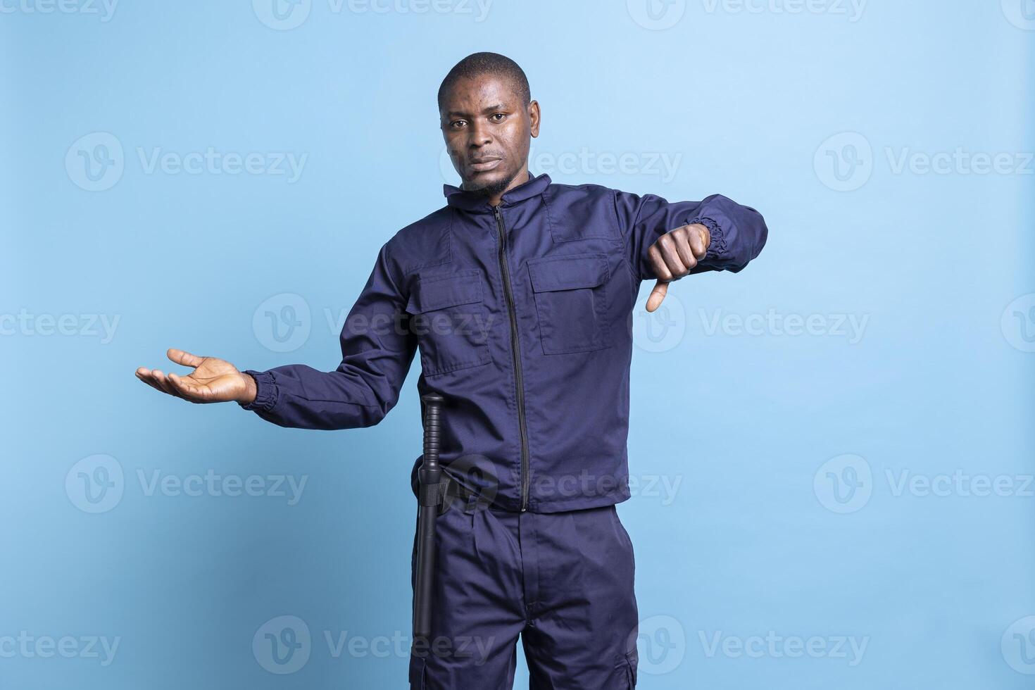 Serious security agent does a dislike thumbs down gesture in studio, presenting his disapproval and acting displeased about bad news. Male bodyguard shows disappointment, negative sign. photo