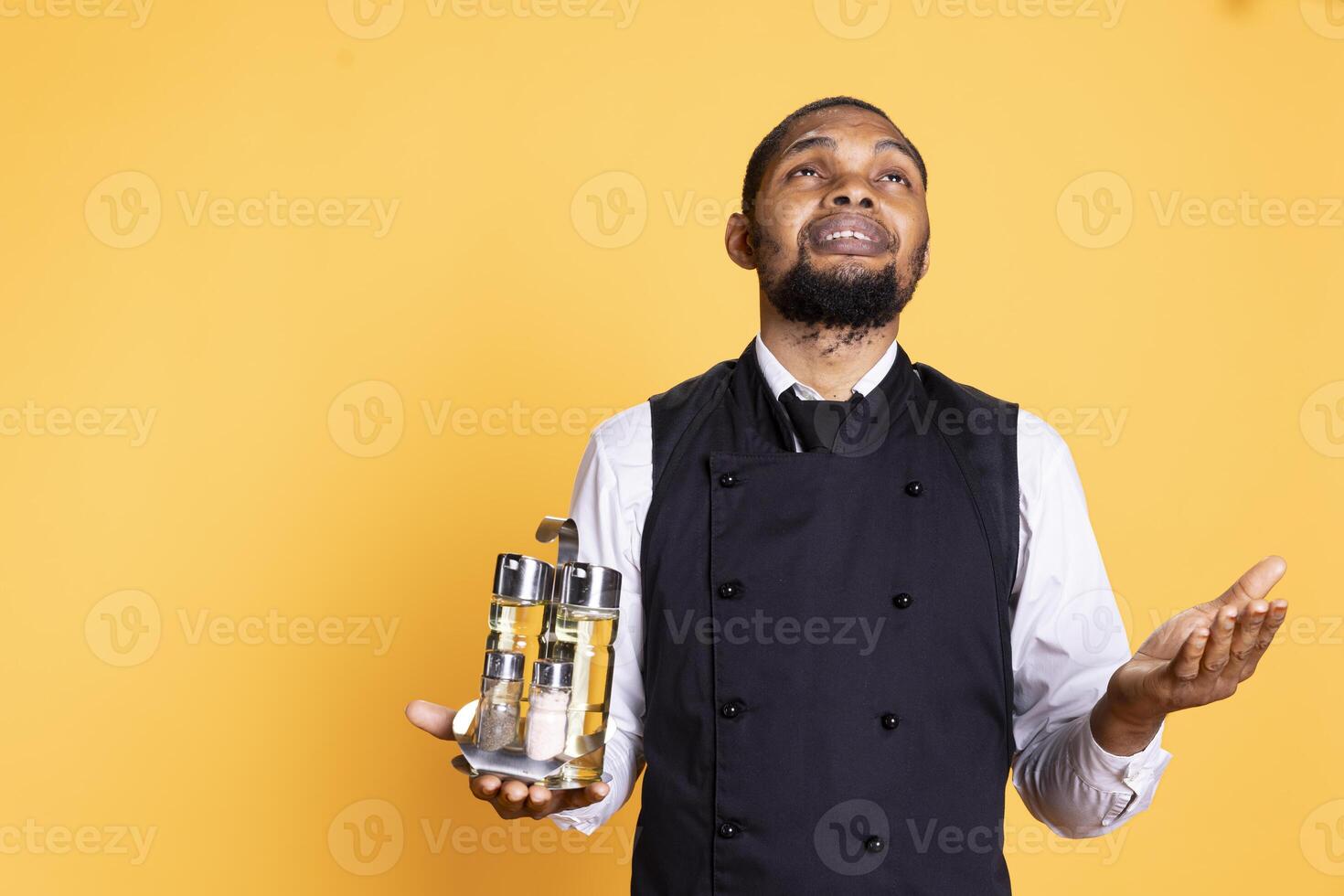Restaurant waiter praying to God before starting a new shift at work, having belief in Christianity and being a religious person. Spiritual butler server in apron carrying cruet set. photo