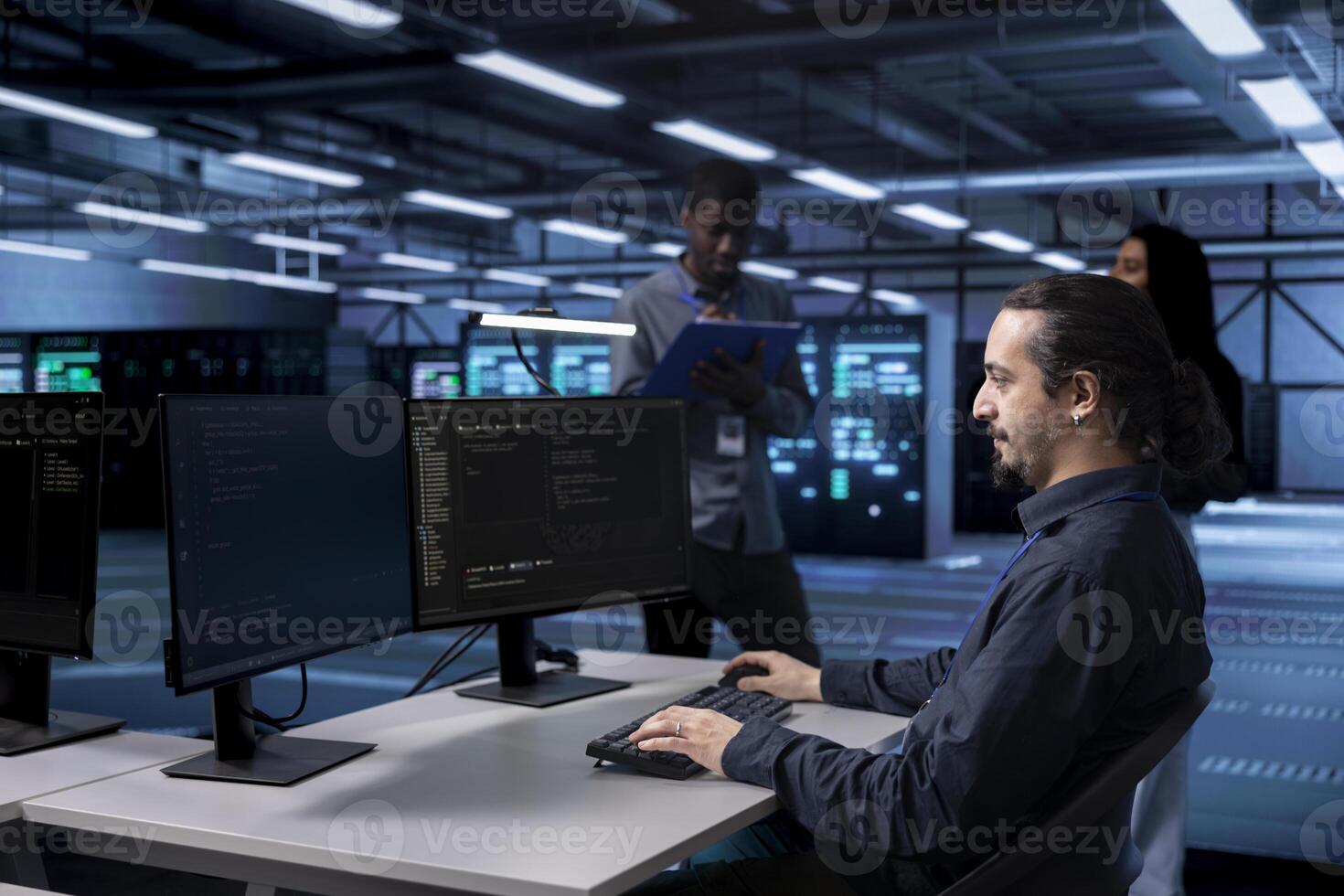 Multiracial team in data center facility running system diagnostic tests on computers. Diverse employees in server farm establishment deploying error checking utilities to mend network issues photo