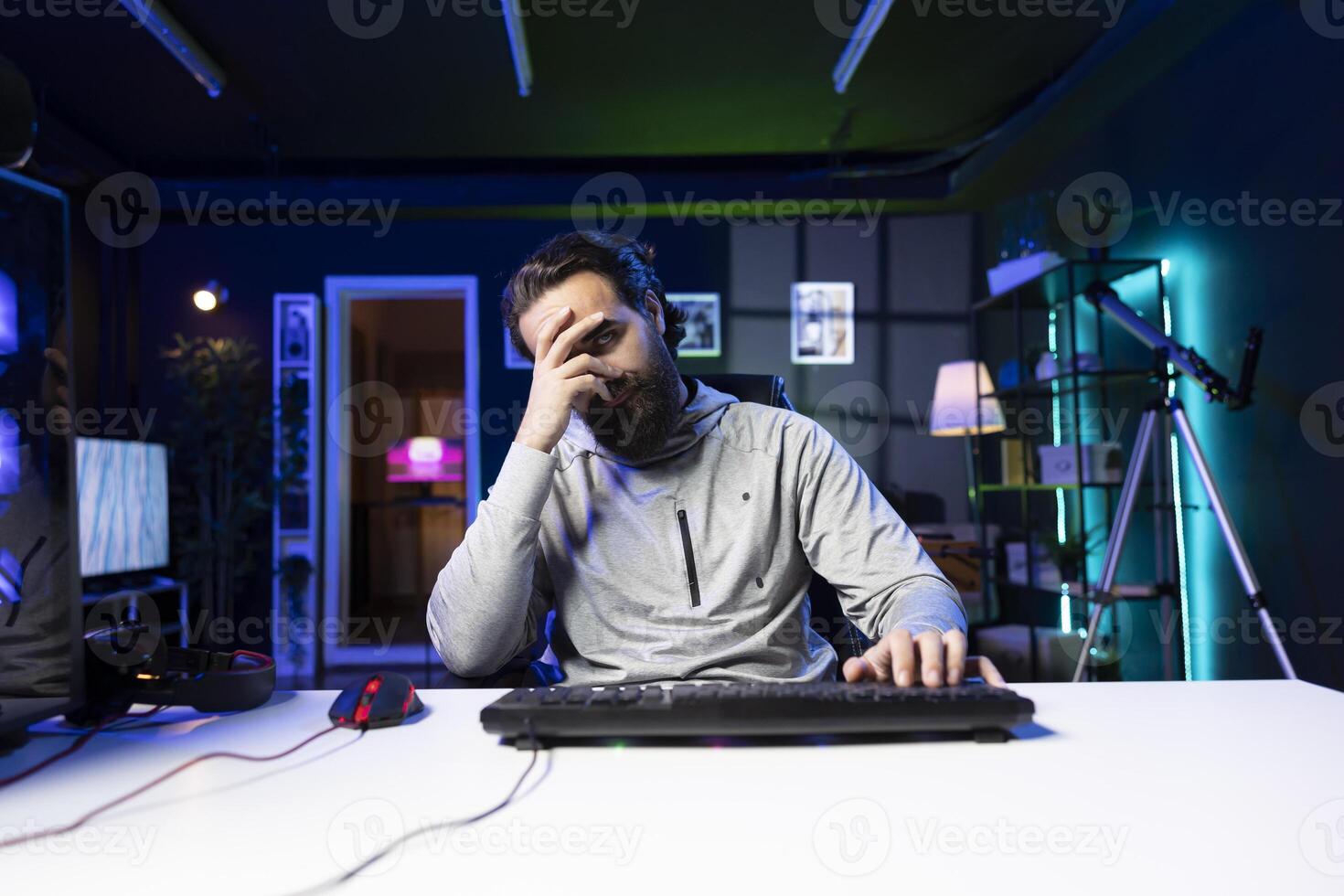 Upset man playing videogames at home, spamming keyboard buttons trying to defeat enemies and avoid defeat. Competitive pro gamer struggling to win online multiplayer esports tournament, feeling sad photo