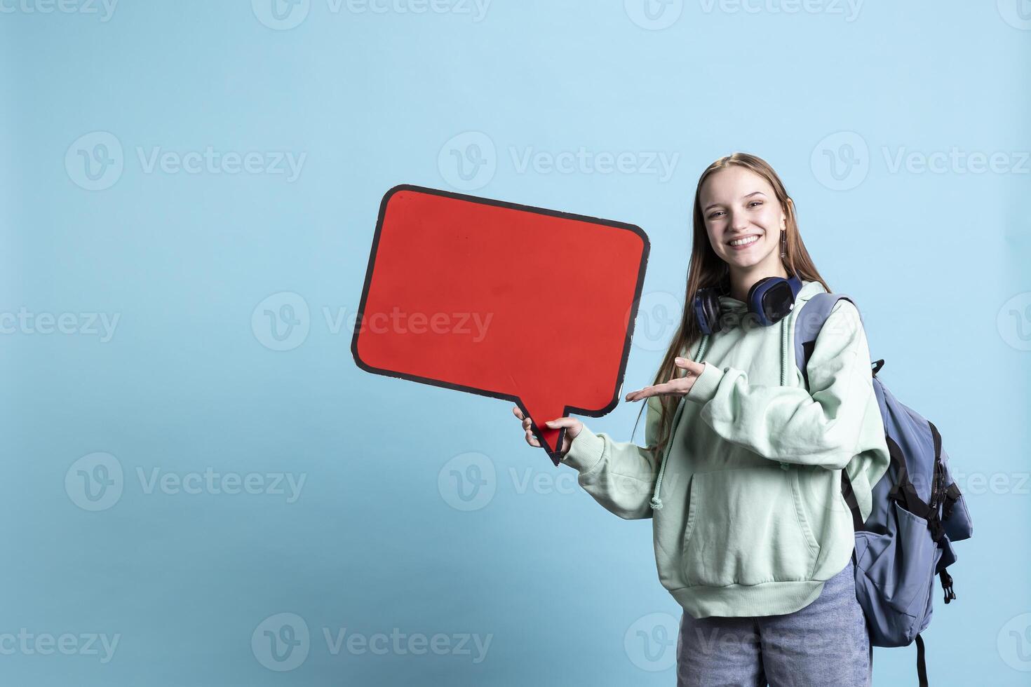 Smiling woman holding red speech bubble sign of empty copy space for message. Joyous teenager presenting thought bubble cardboard used as promotion concept, isolated over studio background photo