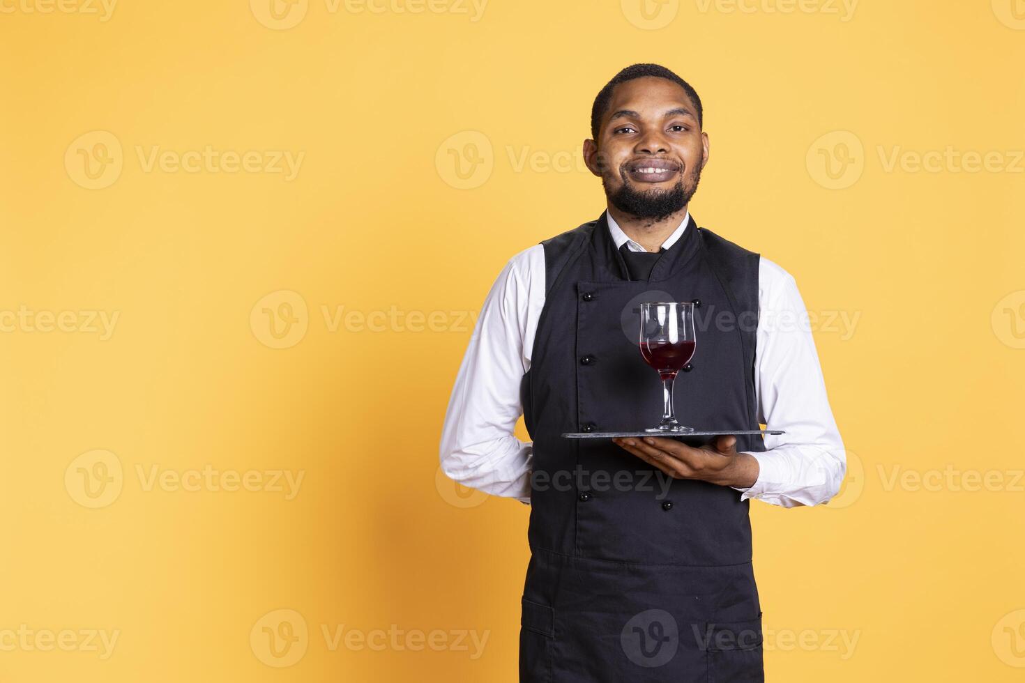 Waiter offering a glass of wine to customers waiting for their food at the table, providing excellent service at a restaurant. Professional staff with uniform bringing drinks to clients. photo