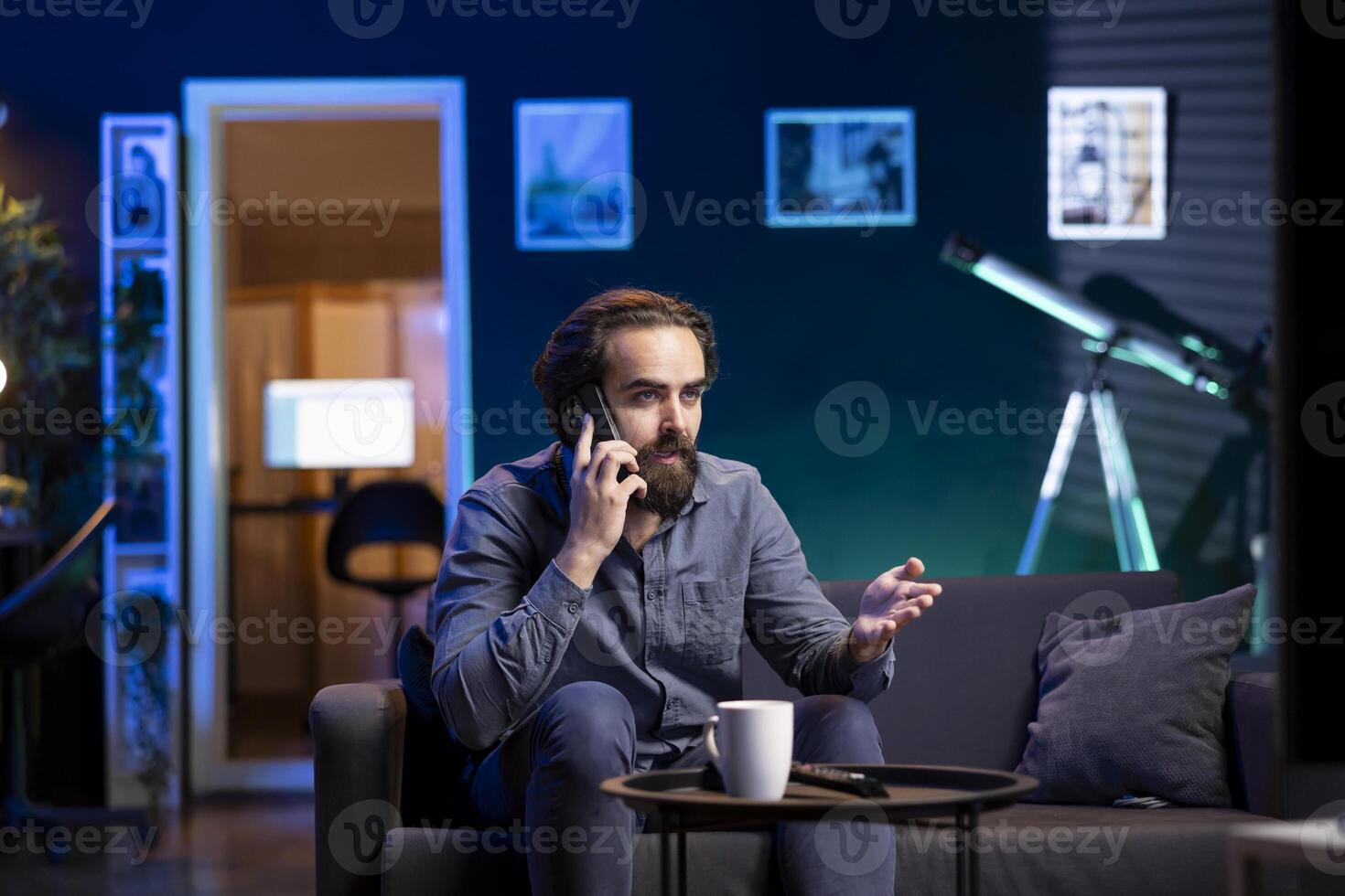 Person on couch binging series on streaming service, talking on mobile phone with friend. Relaxed man watching shows on television, discussing them with mate during telephone call photo