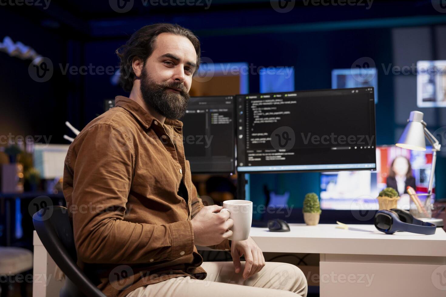 Portrait of cheerful computer engineer enjoying hot beverage while implementing security measures to protect company systems and data. Smiling IT worker drinking coffee and debugging code photo
