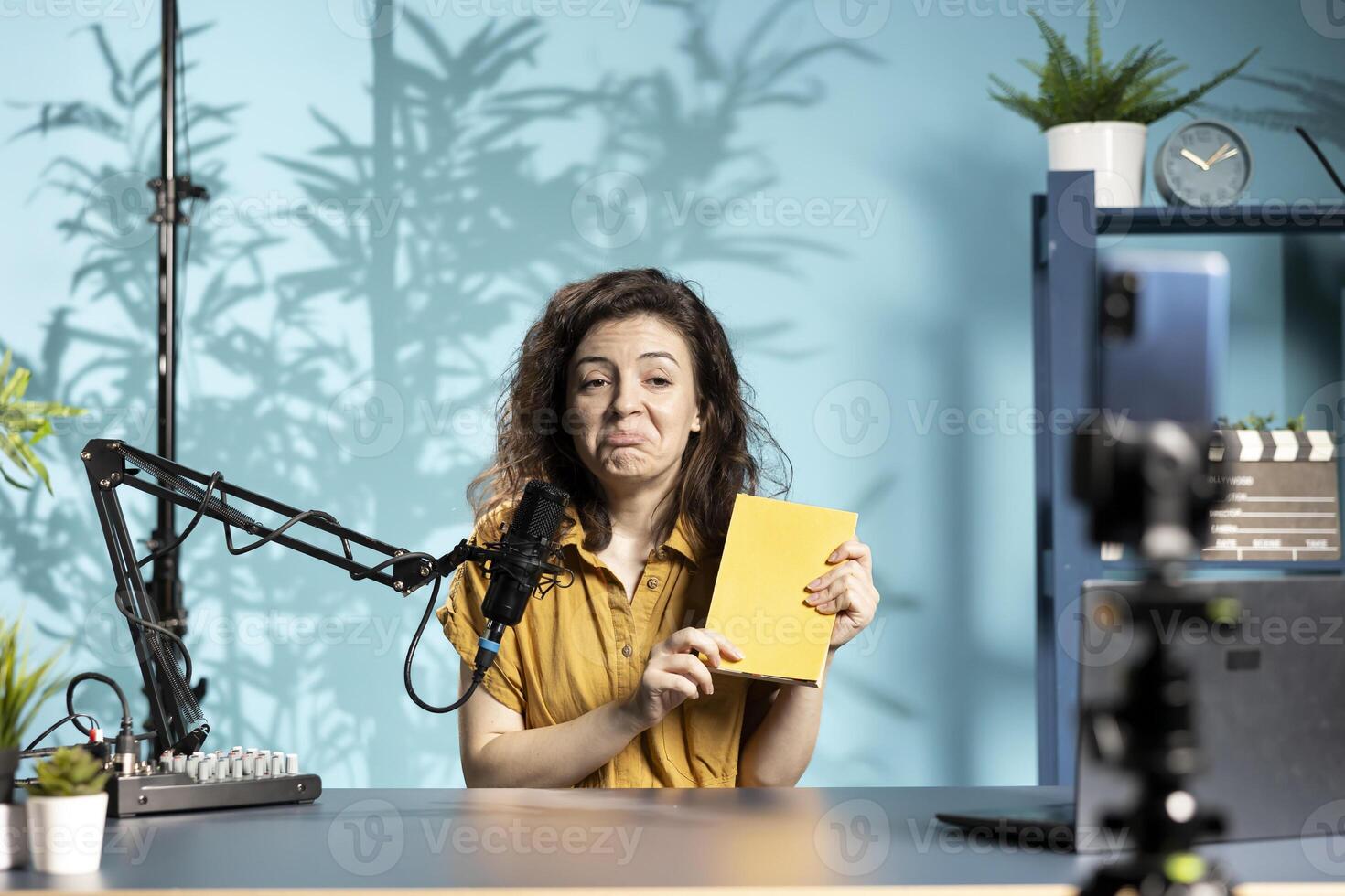 Disappointed woman filming review of book, browsing through pages, unimpressed by weak story. Reviewer frowning, giving her impressions of new novel release to readers, having negative feedback photo