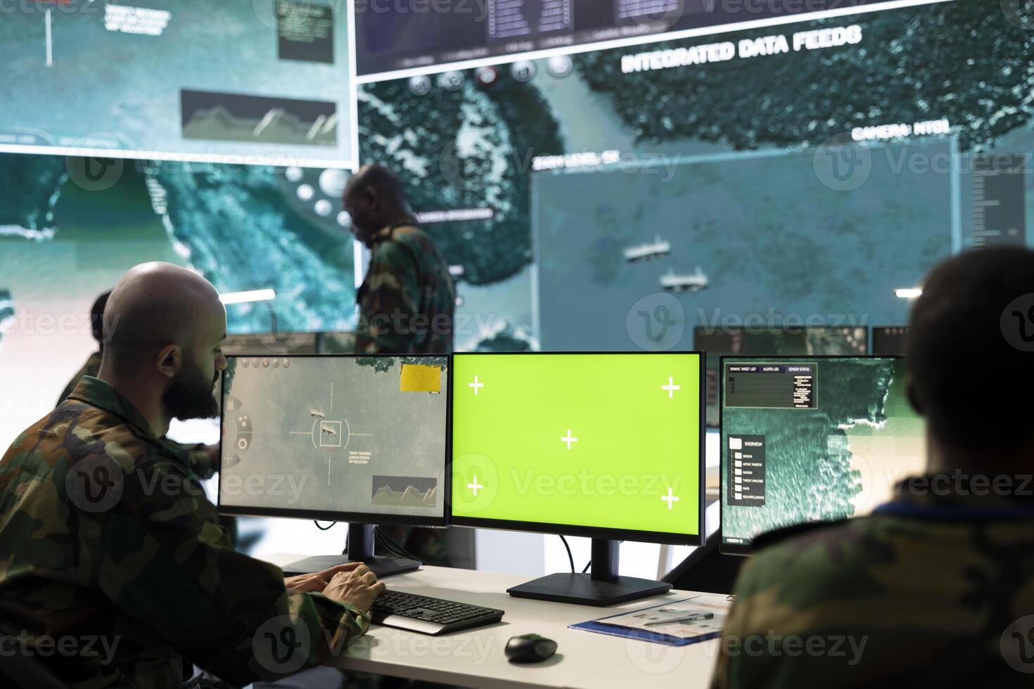 Army soldier working with an isolated pc display next to satellite footage, monitoring CCTV surveillance imagery to ensure national safety in command post. Trooper works on a mission. photo