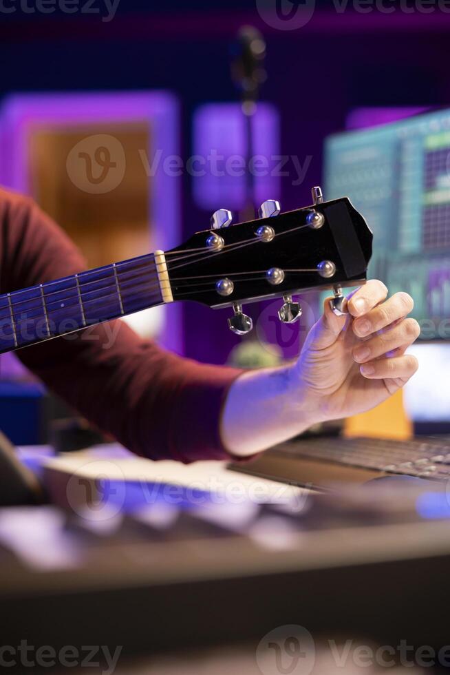 Musician tuning his acoustic guitar to play and record new tunes, working in his home studio to create new music. Songwriter artist playing instrument with mixing and mastering gear. Close up. photo