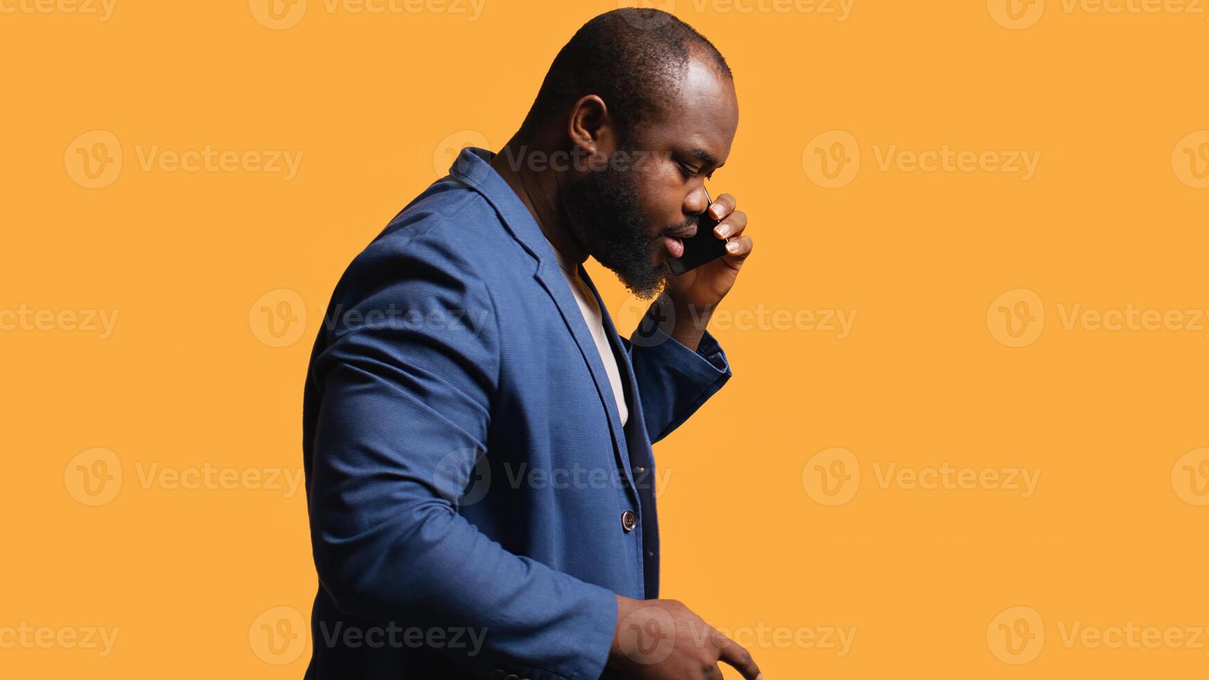 African american man enjoying talking with friends phone call using smartphone, studio background. BIPOC person walking around conversating during telephone call, camera B photo
