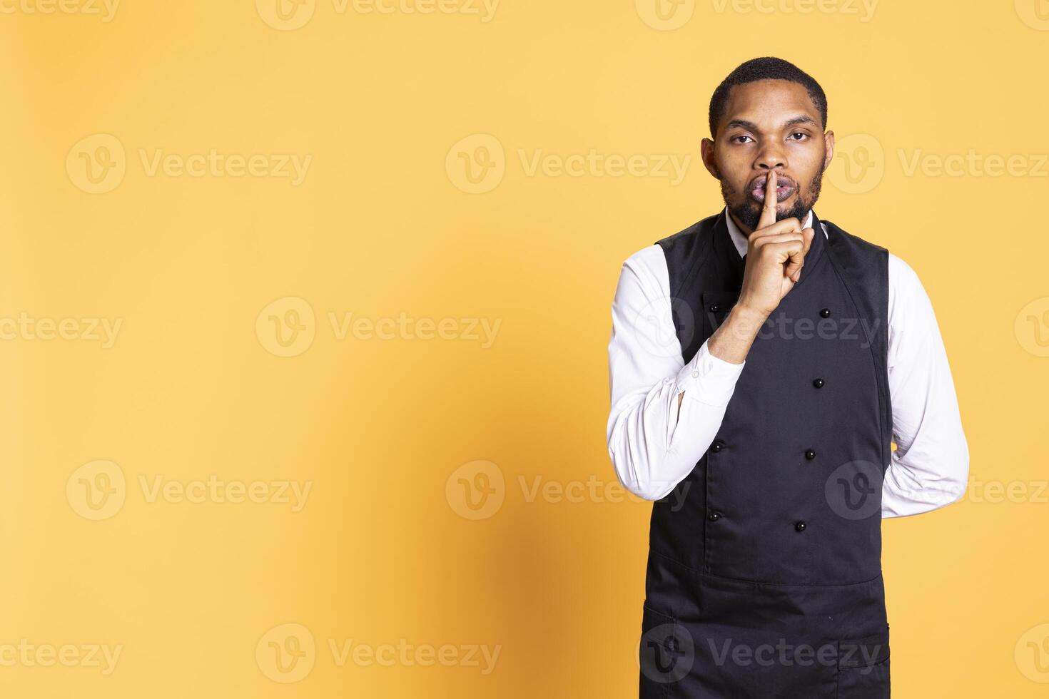 Restaurant butler showing the mute symbol to be quiet and keep secret, covering his lips with his finger. Waiter asking for privacy and secrecy, confidential information and no noise. photo