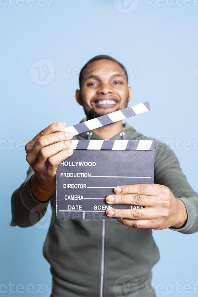 African american positive guy presenting his filming slate for movie industry, cinematography and entertainment with the producer or director clapperboard. Happy confident filmmaker. photo